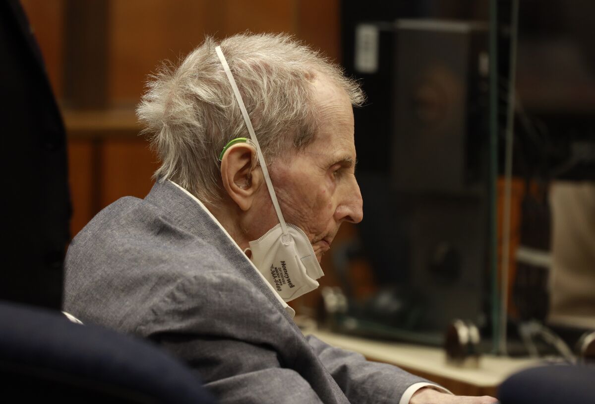 Robert Durst looks down with a mask around his chin while sitting in court