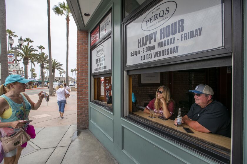 HUNTINGTON BEACH, CA - JULY 01: Lisa and Todd Smith, right, of El Dorado Hills, enjoy drinks as they greet a passer-by who said she can't get used to wearing a protective mask on Main Street Wednesday, July 1, 2020 in Huntington Beach, CA. Bars across Orange County, many of which have only recently reopened, will be forced to shut down again beginning at midnight Thursday, officials announced. County officials on Wednesday announced the closure of bars, pubs, breweries and brewpubs that do not offer dine-in meals amid a troubling surge in coronavirus cases that has resulted in an increased hospitalization rate and the placement of the county on Gov. Gavin Newsom's watch list. (Allen J. Schaben / Los Angeles Times)