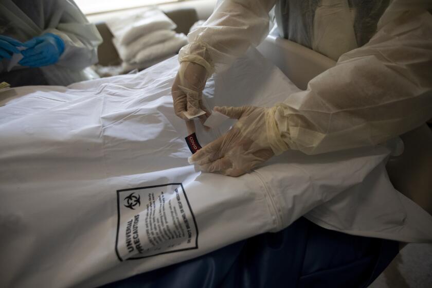 MISSION HILLS, CA - DECEMBER 31: Nurses place a "covid patient" label and covid stickers on the white bag containing a deceased patient. Three people passed way this morning on this one hallway in the covid ICU of complication of covid at Providence Holy Cross Medical Center on Thursday, Dec. 31, 2020 in Mission Hills, CA. According to the 11 Providence Hospitals they have 1560 patients with Covid, 65 awaiting results this morning. Providence has 11 hospitals in Los Angeles, Orange County and the high desert area of San Bernadino. (Francine Orr / Los Angeles Times)