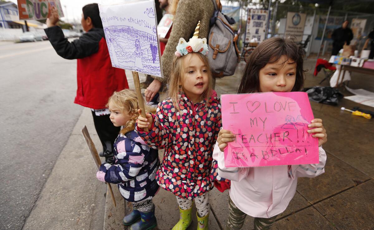 Kindergarten students Isabella Dam, right, and Ava Berg, joined by sister Silke Berg, left, hold signs to support their teacher outside Westminster Elementary School.