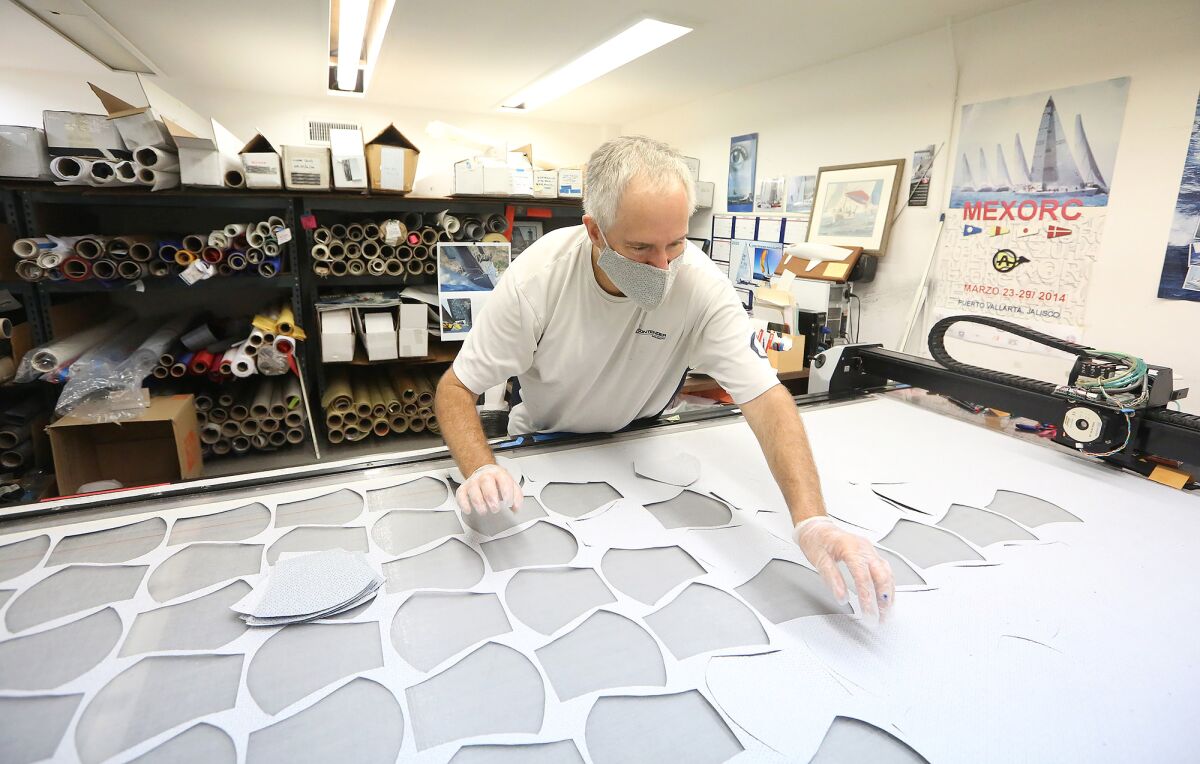 Ken Cooper removes the cutouts, which are the first process in making face coverings, on a vacuum table at the Ullman Sails Newport Beach workshop in Santa Ana on Wednesday.