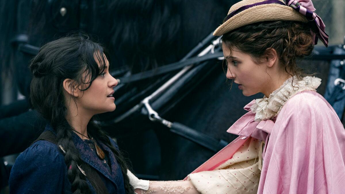 Two young women in 19th century dresses stand face to face, looking anxious