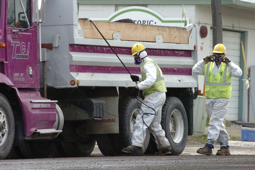 ARCHIVO - Trabajadores de carretera visten trajes protectores contra una posible contaminación por asbesto cuando cargan material de un proyecto de repavimentación en el centro de Libby, Montana, el 28 de abril de 2011. (AP Foto/Matthew Brown, archivo)