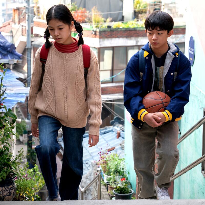 A girl and a boy, he carrying a basketball, walk up an outdoor staircase.