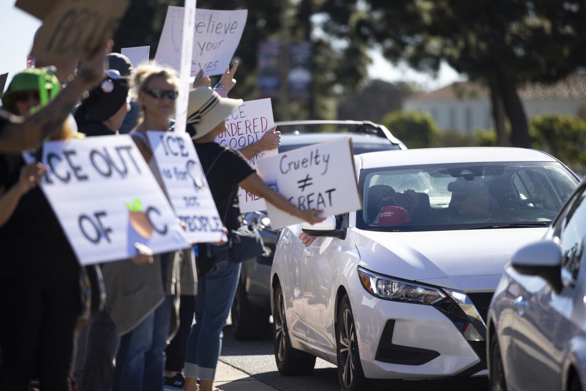 A car with a MAGA hat on the dashboard passes an "ICE Out" protest.