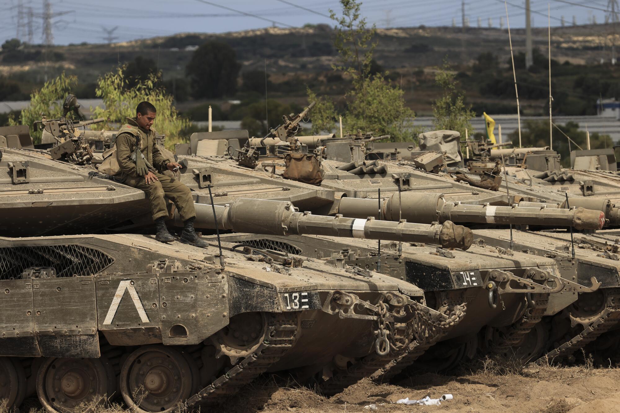 A soldier sits atop one of a row of tanks.