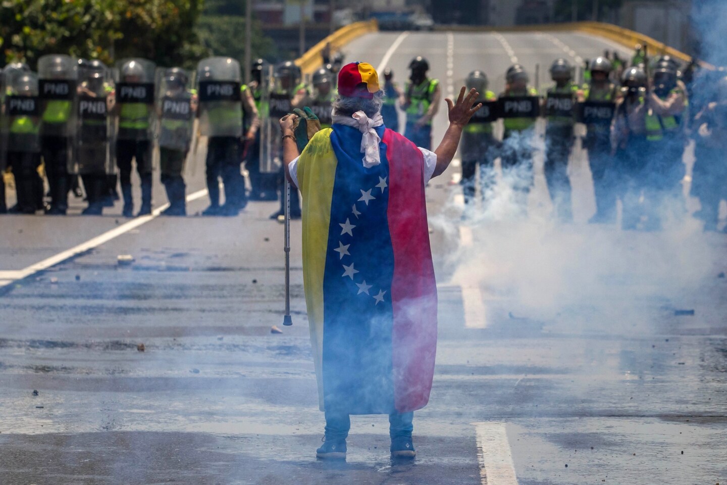 A man draped in the Venezuelan flag faces off with Bolivian National Police as demonstrators and police clash in opposition protests in Caracas, Venezuela. Thousands of Venezuelans are once again taking to streets in protest against the government of President Nicolas Maduro.