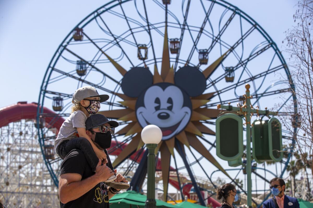 A boy rides on his father's shoulders as they pass the Ferris wheel at Pixar Pier.