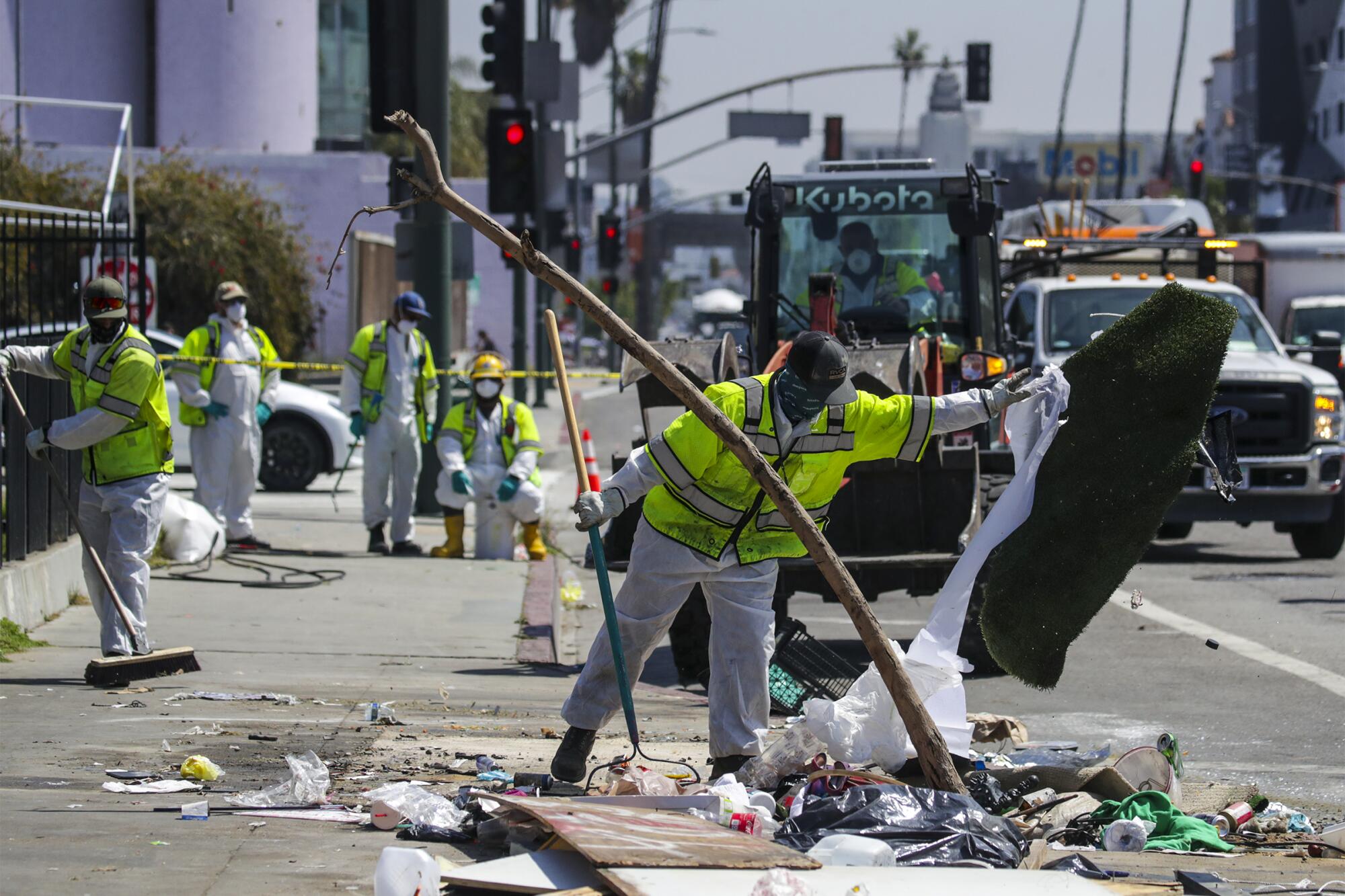 People in yellow vests sweep trash from a sidewalk.