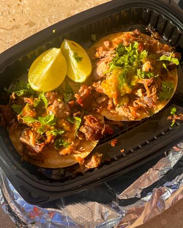 Two carnitas tacos in a to-go container