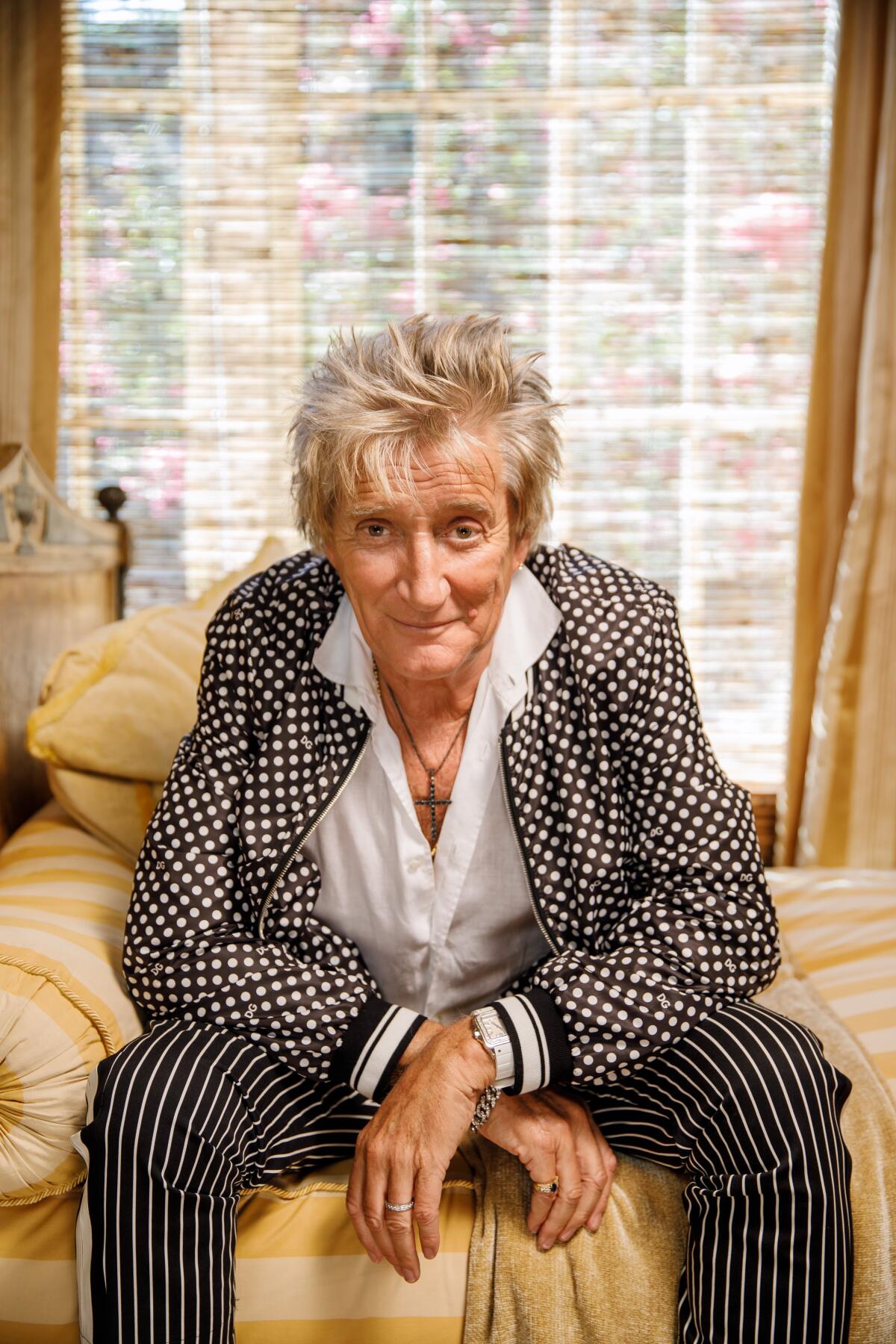 A man in a printed suit leans forward while sitting on furniture 