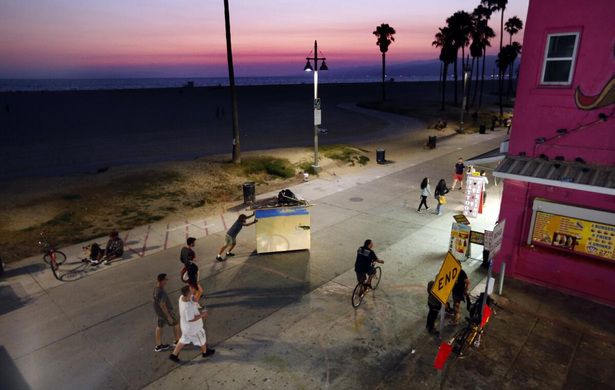 Chris Buck, who has been homeless for the last year, wheels his portable home along the Venice boardwalk as night falls.