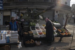 A man looks at white crates of fruits and vegetables displayed for sale in front of a tank