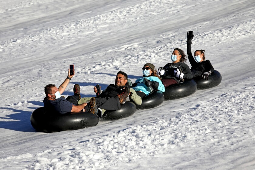 Tubers slide down a snowy slope, all but one in masks.