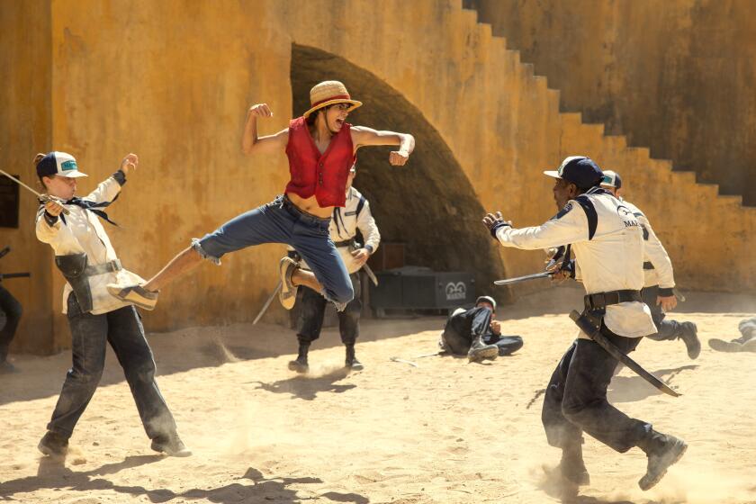 A young man in a straw hat, red vest and jean shorts in mid-air kicking and punching two people in a white jacket and jeans