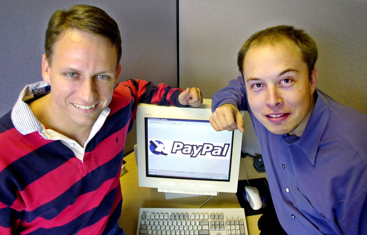 A man in a striped shirt and a man in a button-down shit both lean onto a computer monitor.