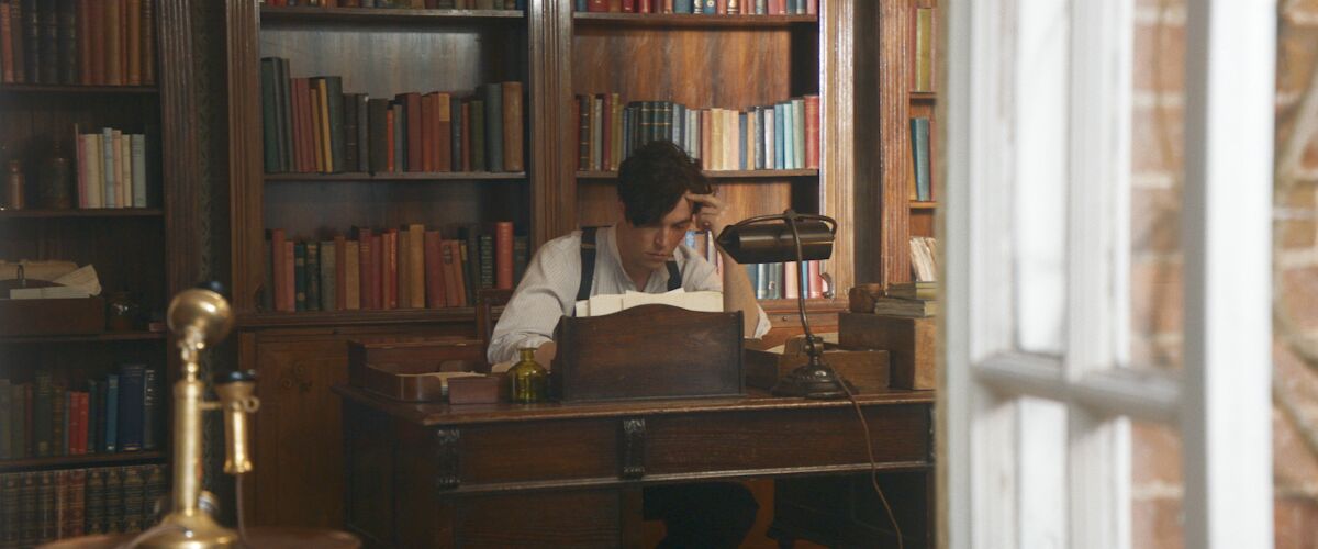 A young man sits thinking at a desk in the movie “The Laureate.”