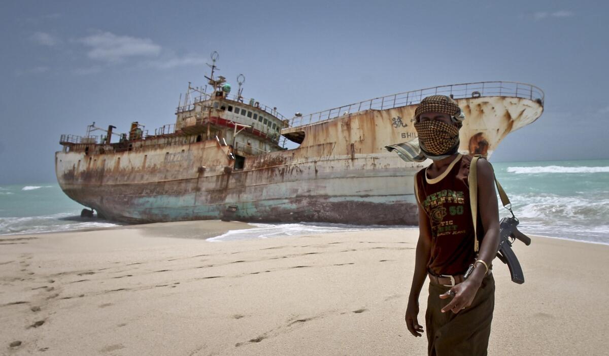 Masked Somali pirate Abdi Ali stands near a Taiwanese fishing vessel that washed up on shore after the pirates were paid a ransom and released the crew in Hobyo, Somalia.