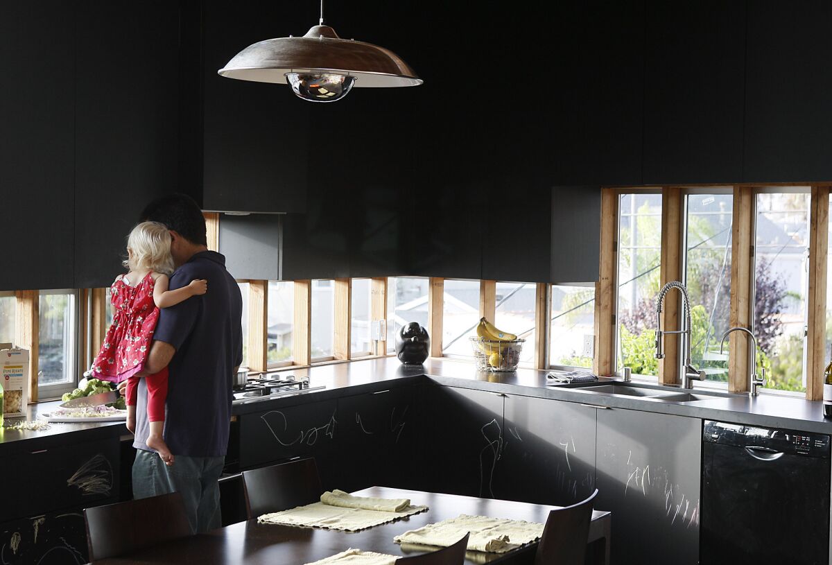 Robert Choeff holds daughter Zara in his Venice kitchen, where the dark cabinets in chalkboard paint leave the emphasis on views and conceal the refrigerator and other appliances. The paint and polished concrete floors make the kitchen feel expansive, even though it's a mere 125 square feet.