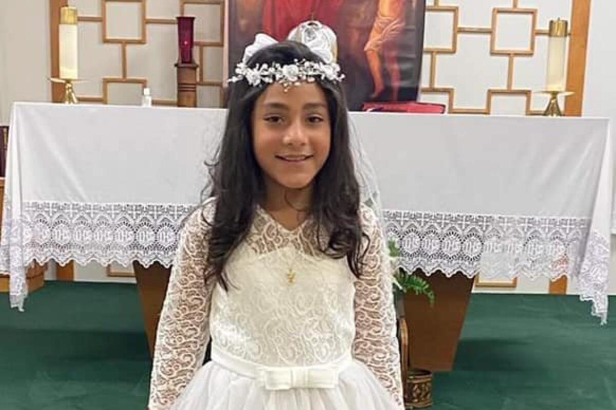 A little girl in a white lace dress and headpiece, standing in front of a church altar