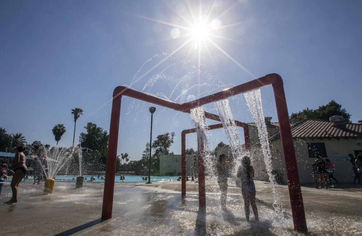 Children play in the water of a park fountain beneath a bright sun.