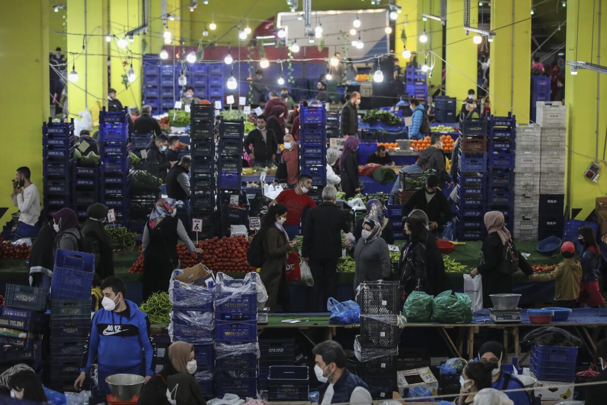 Shoppers throng produce stalls amid stacked crates at a market 