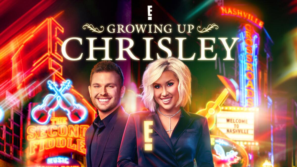 Chase and Savannah Chrisley in dark clothing smiling and posing in front of neon signs 