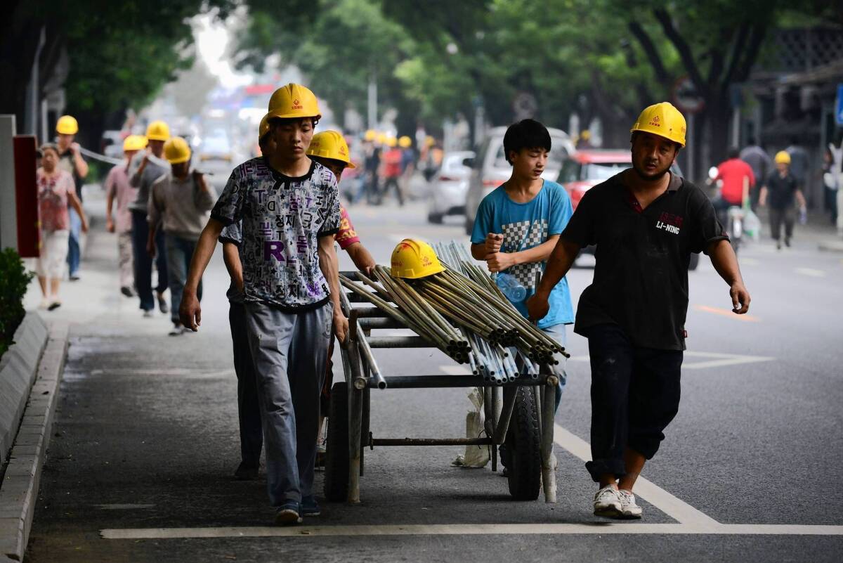 Workers move steel tubes near a construction site in Beijing. In China, reining in credit will squeeze banks and borrowers, including real estate developers.