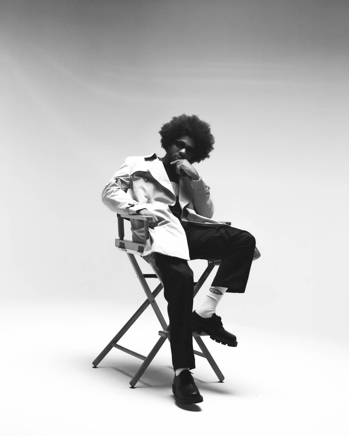 A man with an afro and dark sunglasses sits in a director's chair