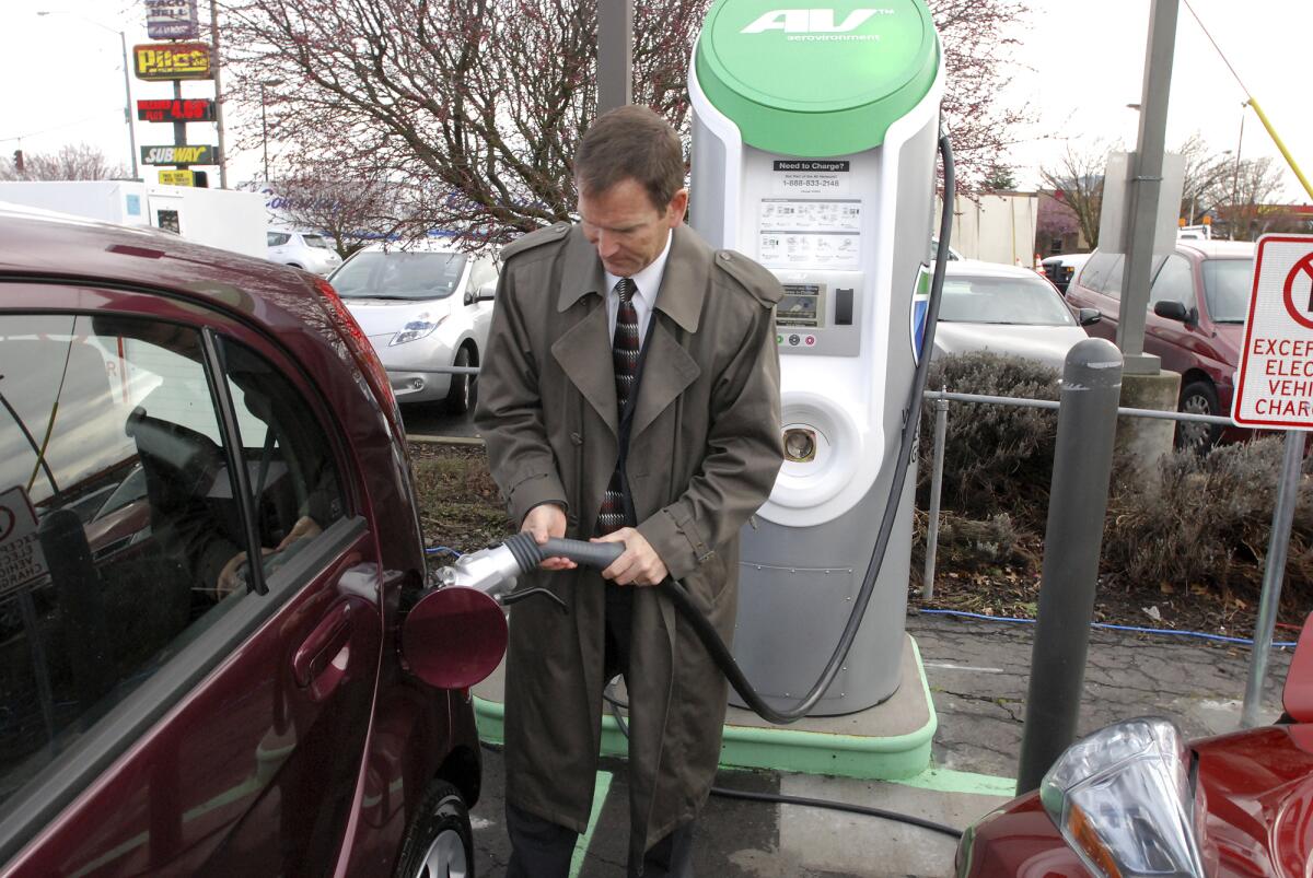 A man in a suit demonstrates the use of a fast-charger connection on a car. 