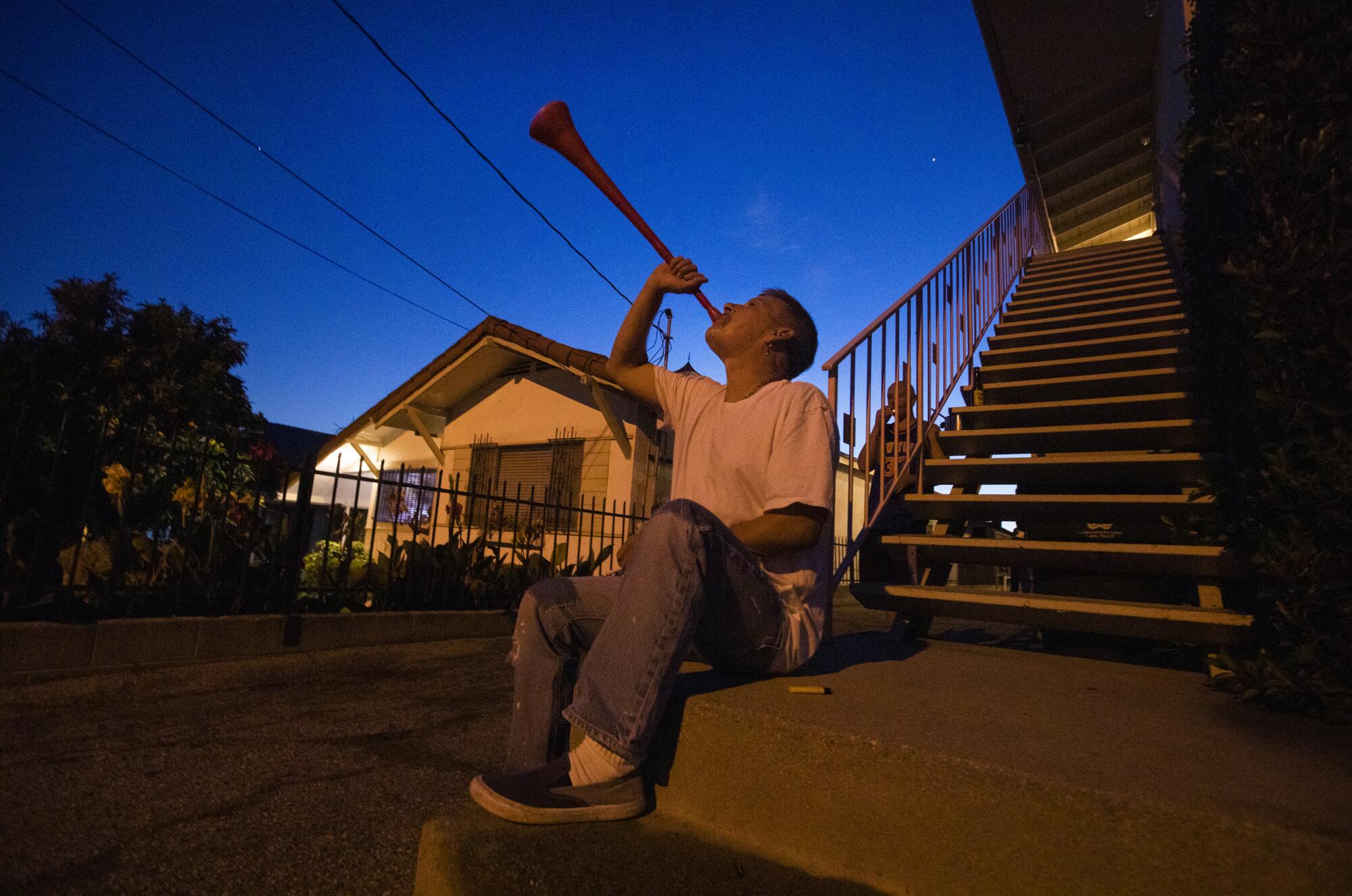 Booka Bickar, 59, makes noise with a plastic horn outside a friend's apartment on Lucile Ave. in Silver Lake, drawing attention to thank essential workers and all the people on the front lines against the coronavirus. Every night for about 5 minutes, starting at 8pm sharp, he and other people on the block and the surrounding area make noise thanking workers.