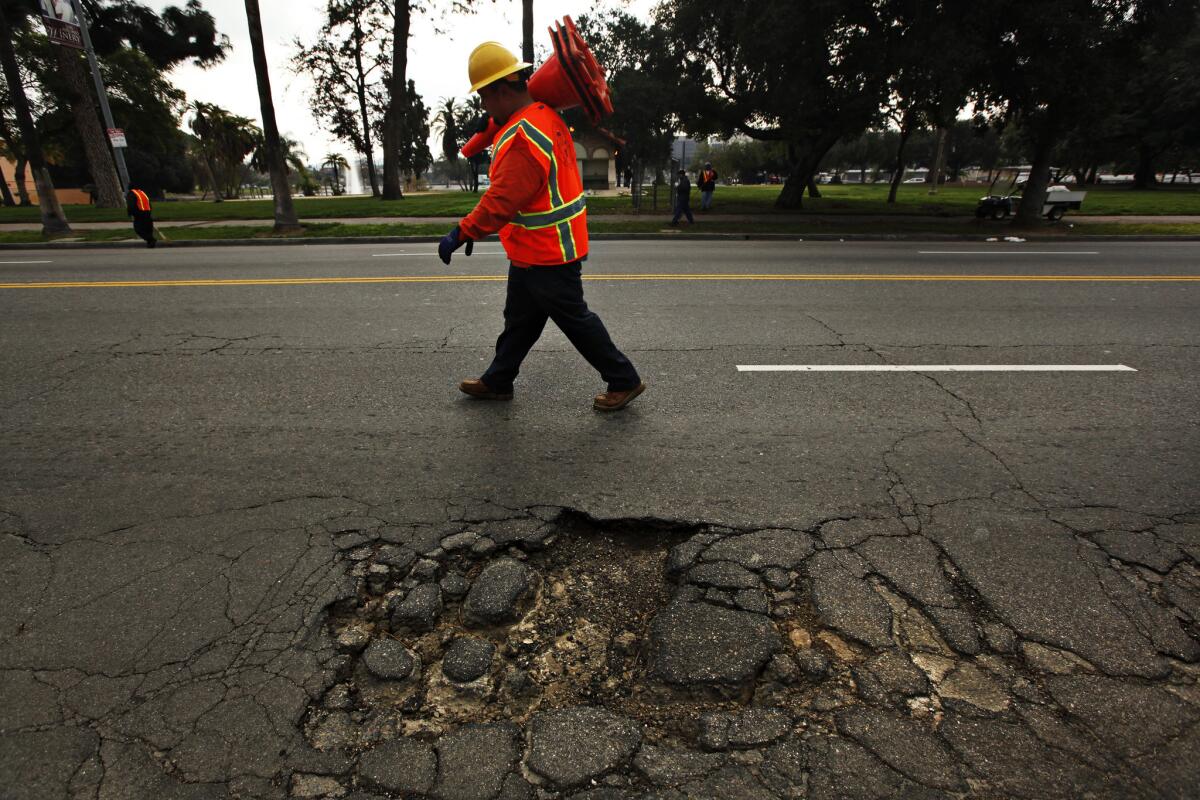 A street worker places cones on the road near a large pothole near Lincoln Park in Los Angeles.