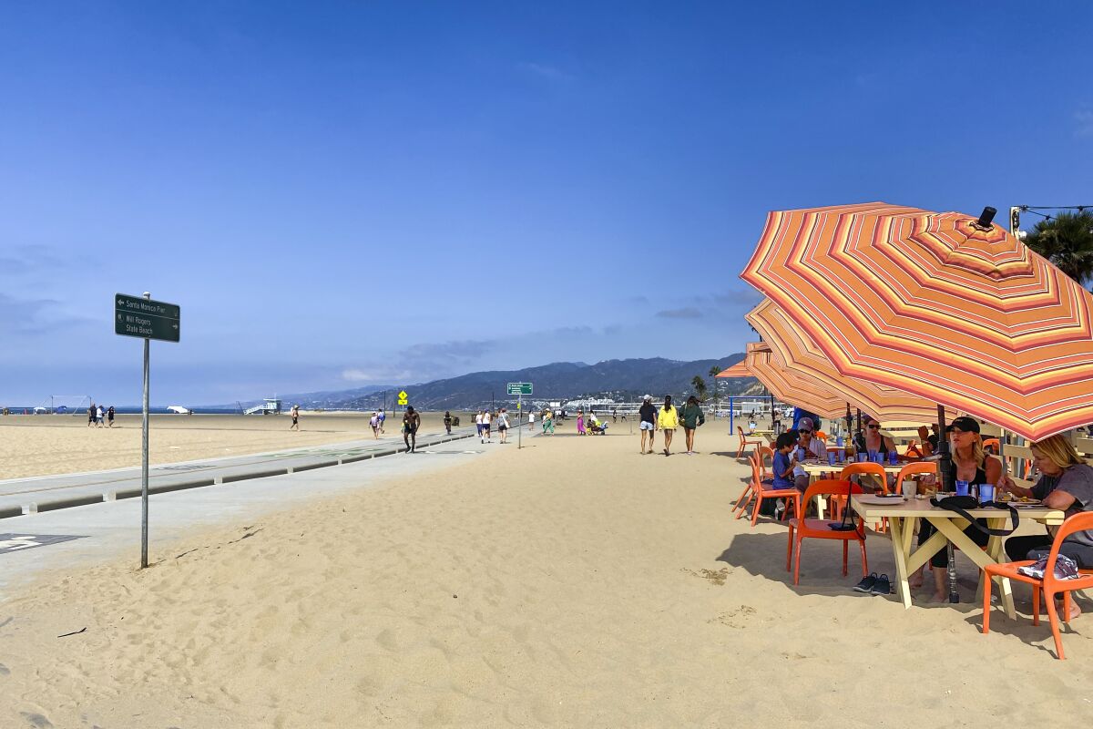People dining at tables with large umbrellas at the beach 