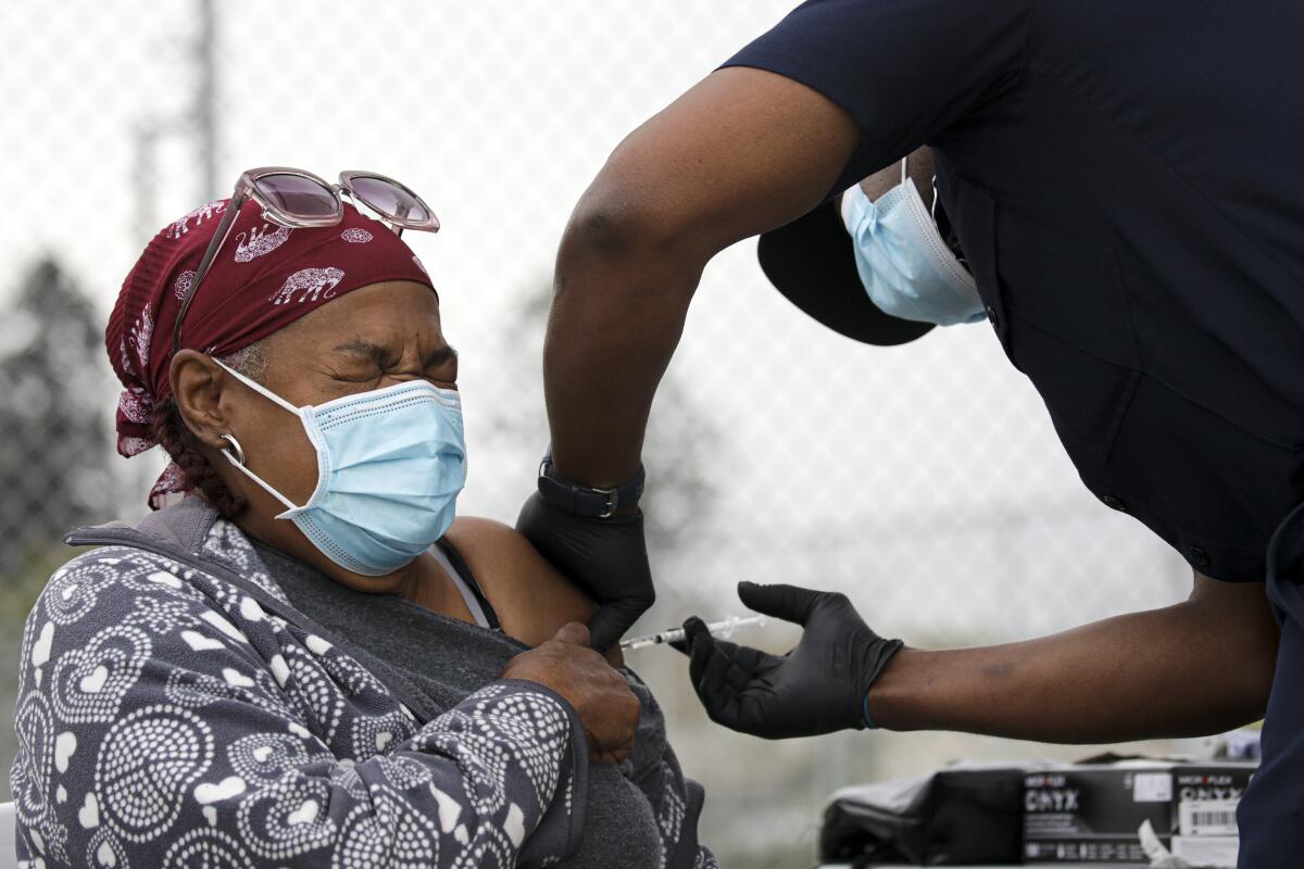 A masked woman winces as she is given a shot in the arm 