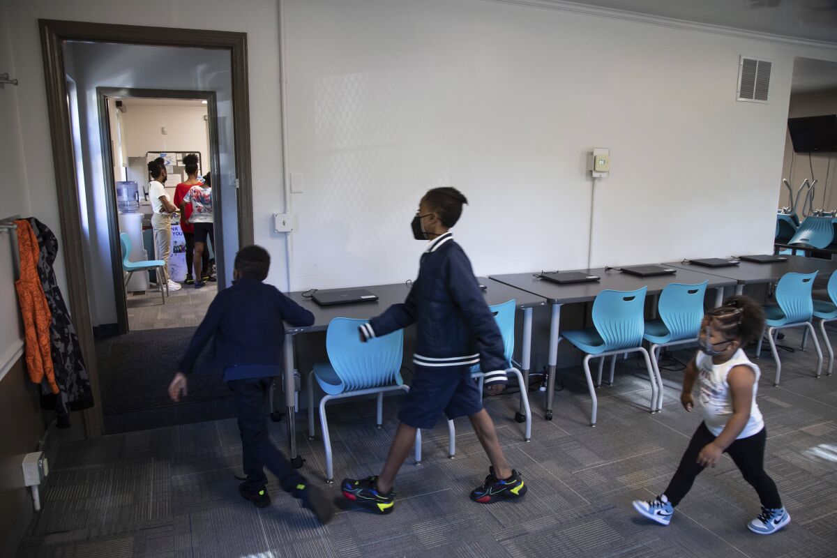 Children walk through a room with laptops, desks and chairs