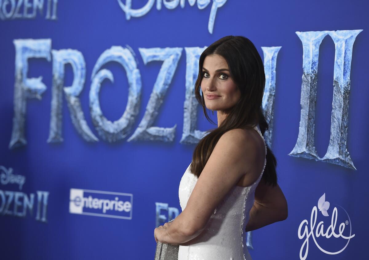 Idina Menzel posing in a white sleeveless dress against a blue background