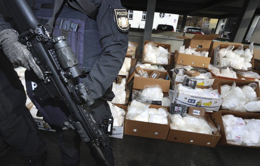 Police officers of the Bavarian riot police stand in front of about 1.5 tons of cocaine that are ready for transport in Bavaria, Germany, Wednesday, Dec.15, 2021. As part of Operation Snow Melt, the Bavarian police destroyed the cocaine at a secret location in a waste incineration plant in Upper Bavaria under the strictest security measures. The narcotics of the highest purity come from various seizures over the past few years. It is the largest drug destruction operation in the history of the Bavarian police.(Karl-Josef Hildenbrand/dpa/dpa via AP)