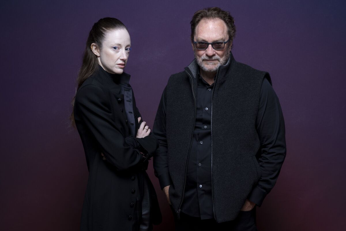 A woman and a man in dark glasses stand together.