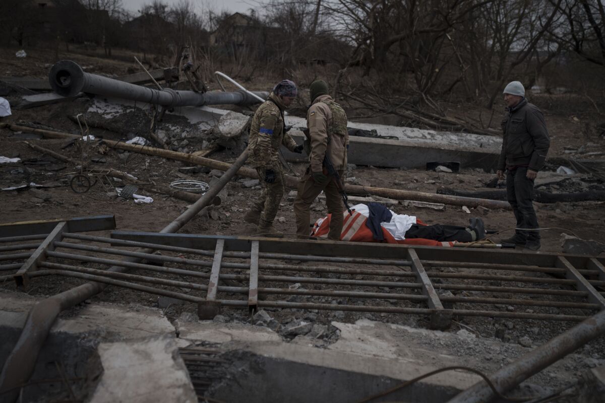 The body of a civilian, whose cause of death is unknown, lays on a stretcher on a path being used as an evacuation route out of Irpin, on the outskirts of Kyiv, Ukraine, Saturday, March 12, 2022. Kyiv northwest suburbs such as Irpin and Bucha have been enduring Russian shellfire and bombardments for over a week prompting residents to leave their homes. (AP Photo/Felipe Dana)