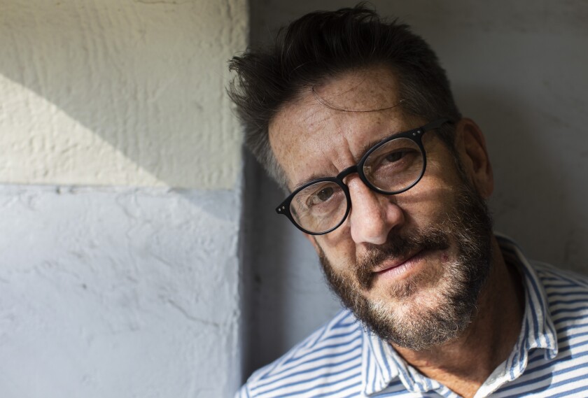 A man in glasses leans against a concrete wall.