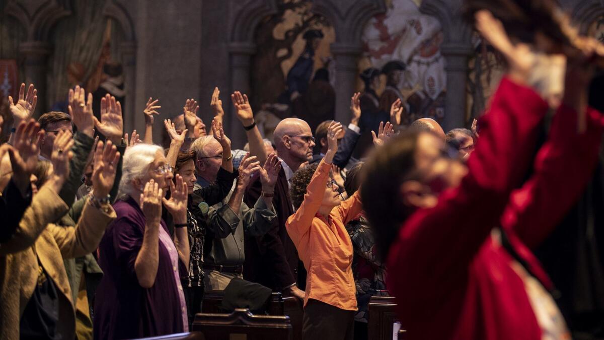 People raise their arms during an interfaith prayer during the Wondering and Commitment ceremony at Grace Cathedral to kick off the Global Climate Action Summit on Wednesday in San Francisco.