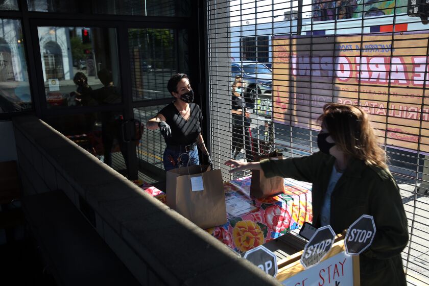 LOS ANGELES, CA - MAY 12: Gretel Diaz, left, hands over a no contact to go order for a customer at Guerilla Tacos on Tuesday, May 12, 2020 in Los Angeles, CA. Guerilla Tacos "serves tacos inspired by the flavors of the city, served on tortillas." (Dania Maxwell / Los Angeles Times)
