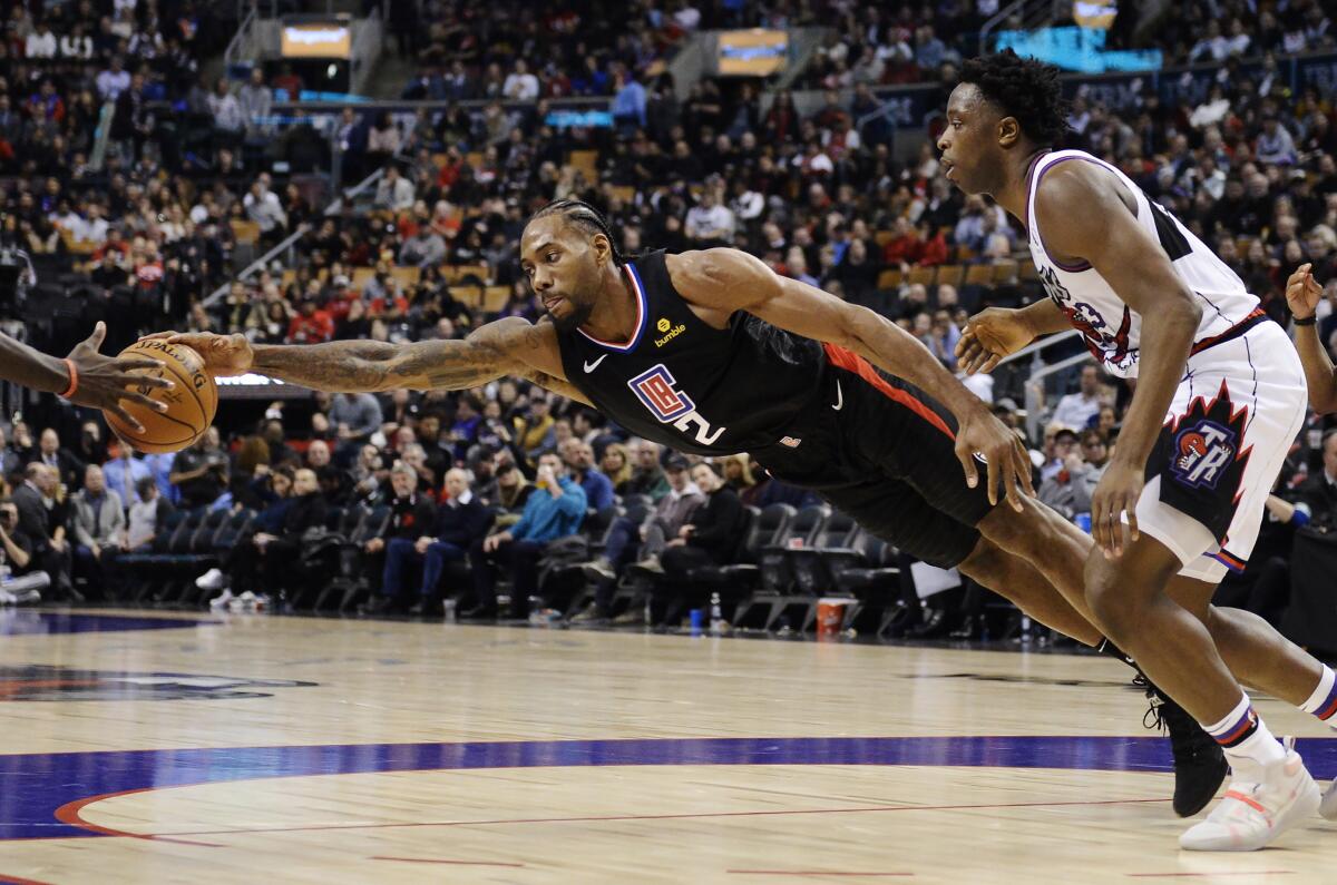 Los Angeles Clippers forward Kawhi Leonard (2) stretches for the ball as Toronto Raptors forward OG Anunoby (3) looks on during the second half of an NBA basketball game, Wednesday, Dec. 11, 2019, in Toronto. (Nathan Denette/The Canadian Press via AP)