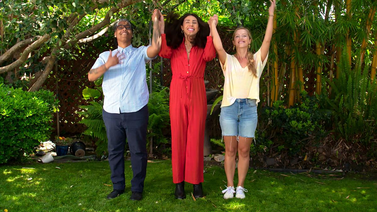 Three people smiling and holding hands lift up their arms.