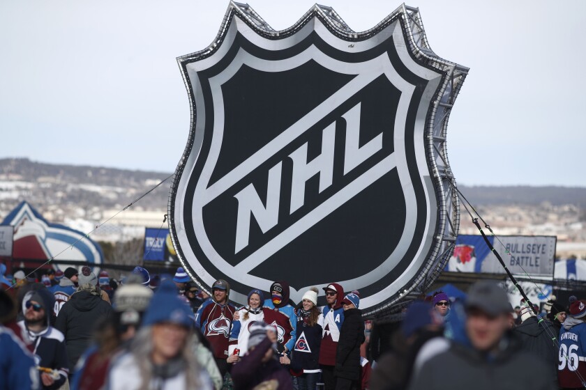 FILE - In this Feb. 15, 2020, file photo, fans pose below the NHL league logo at a display outside Falcon Stadium before an NHL Stadium Series outdoor hockey game between the Los Angeles Kings and Colorado Avalanche, at Air Force Academy, Colo. The NHL announced Friday, Dec. 17, 2021, that it was postponing all games for the Colorado Avalanche and Florida Panthers through at least next weekend amid worsening COVID-19 test results across the league. (AP Photo/David Zalubowski, File)