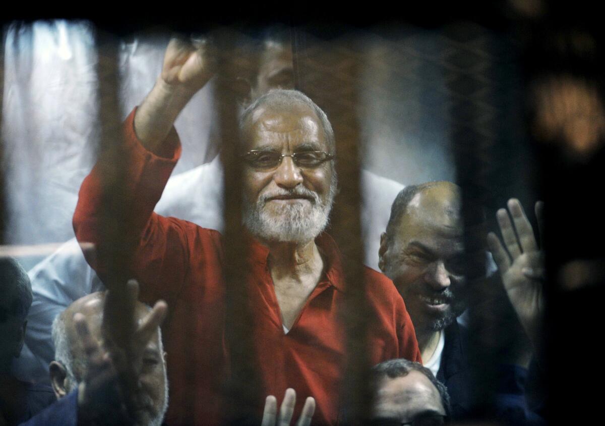 Mohammed Badie and other men, seen through bars, smile and wave.