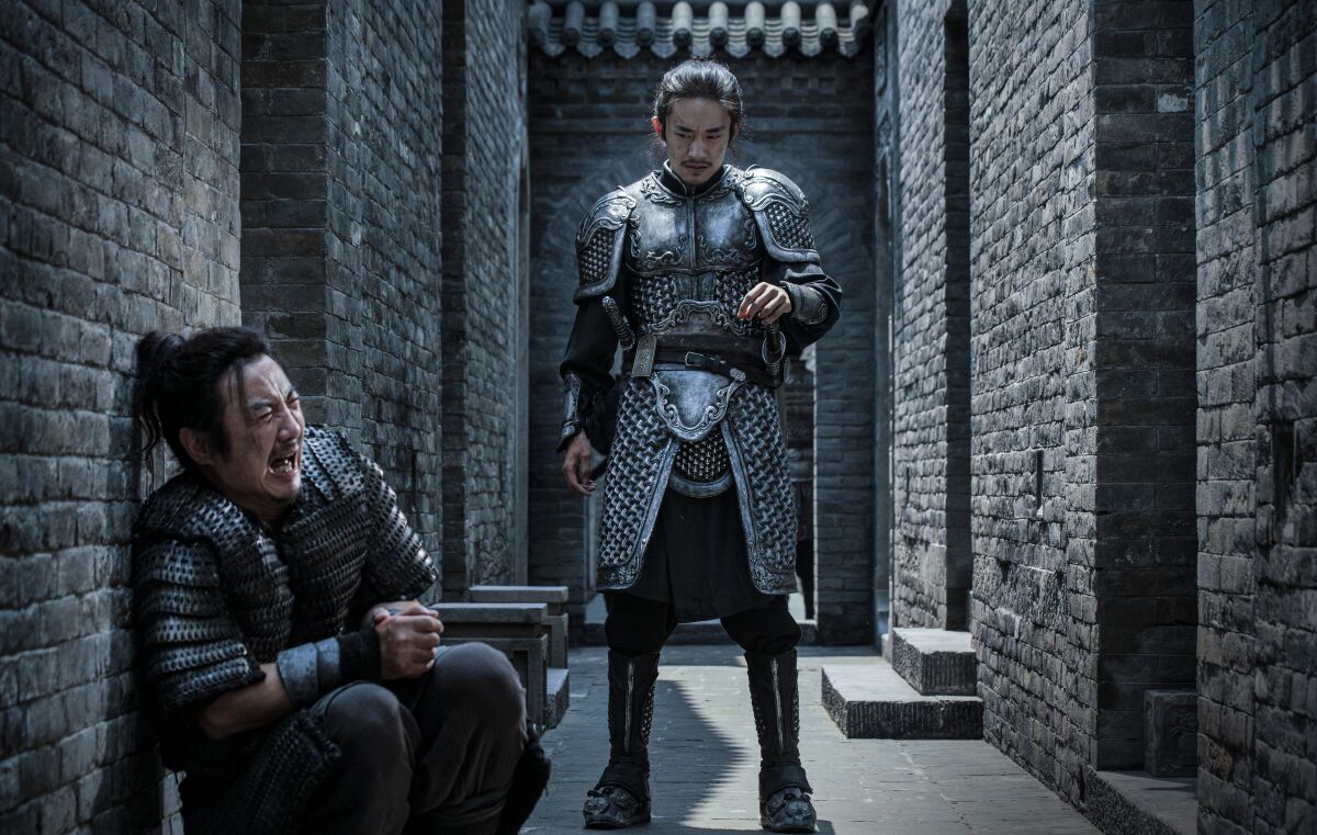 A man in armor stands over a man crouching in an alley
