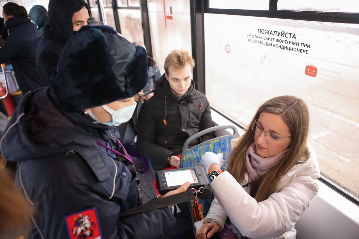 A masked worker scans a code on a woman's wrist on a train.