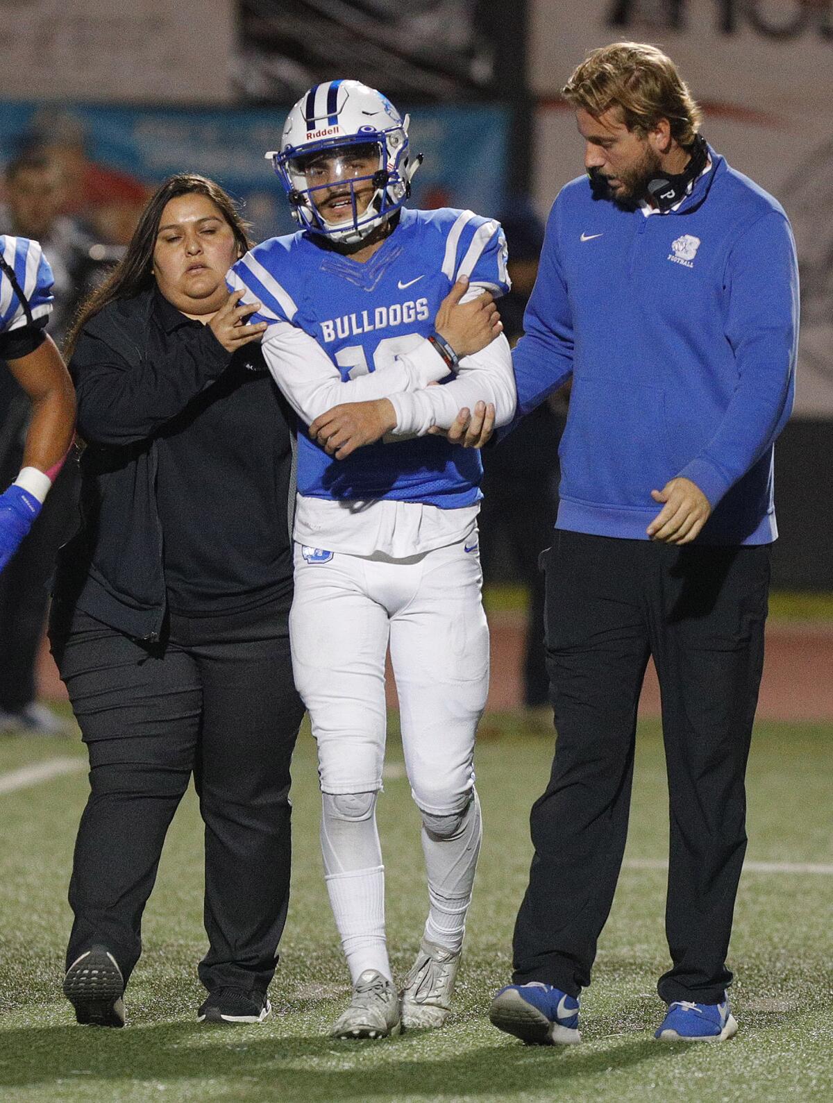 Burbank's quarterback Aram Araradian is helped off the field by an athletic trainer and Burbank's head coach Adam Coleman after being injured during a play against Muir in a Pacific League football game at Burroughs High School on Monday, October 14, 2019. He did not return to the game.