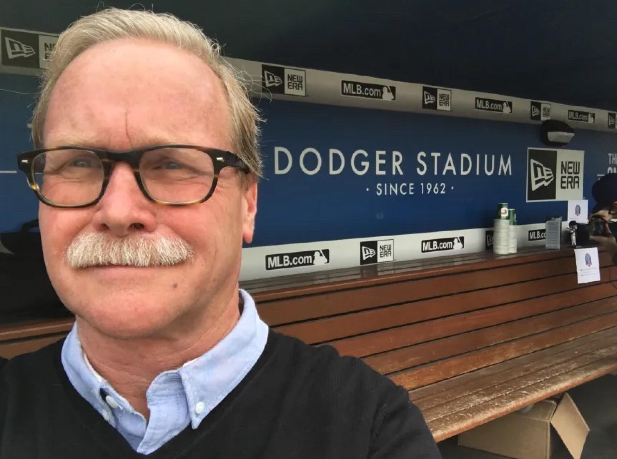 A man with a white mustache stands in front of the L.A. Dodgers dugout.